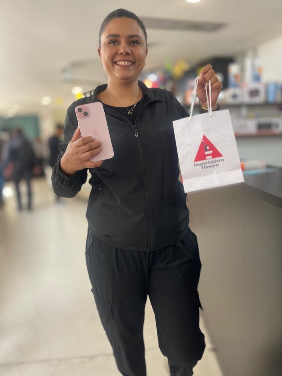 Cliente sorrindo com iPhone e sacola da Importadora Mineira